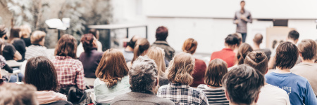 An image taken from the back of a lecture room with people sitting in chairs